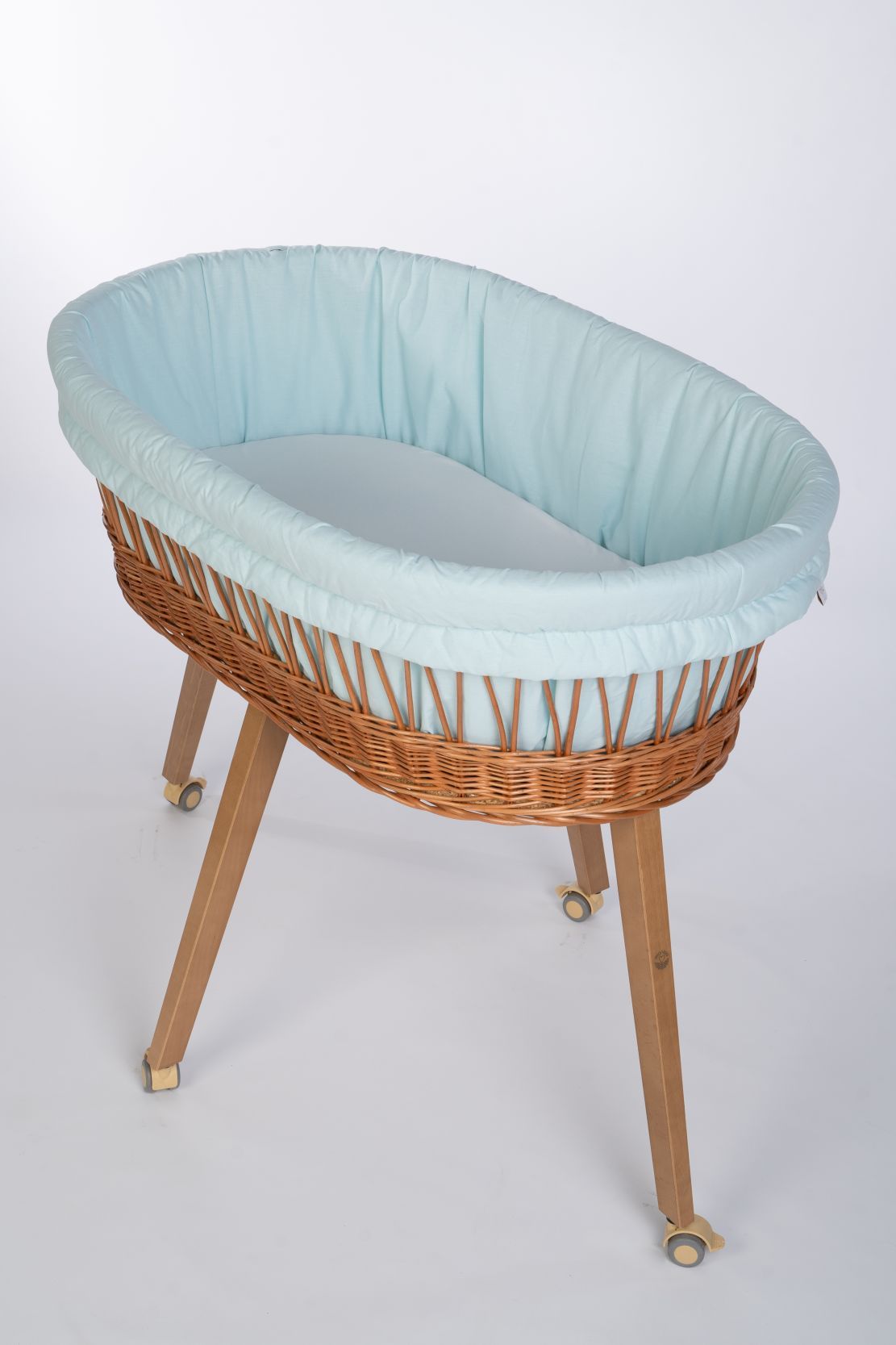 Light blue cotton Stubenwagen polster with padded sides in woven wicker basket on wooden legs with wheels. - Mionido - Stubenwagenpolster (Baumwolle)